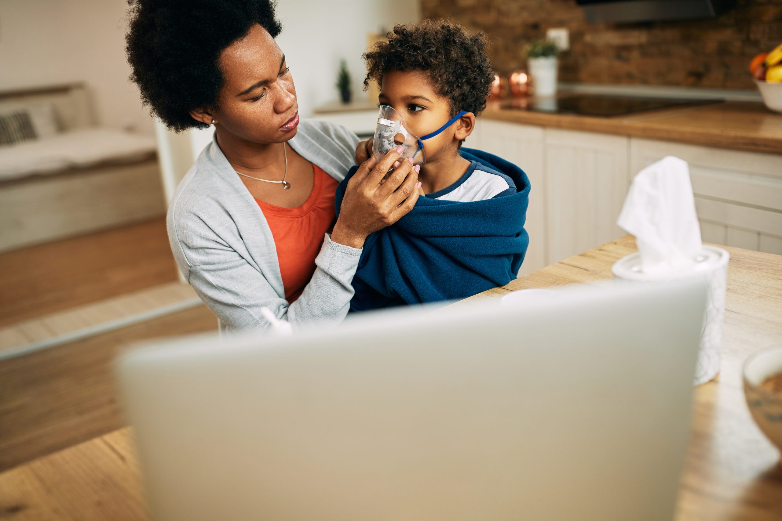 Black mother using nebulizer during inhaling therapy of her ill