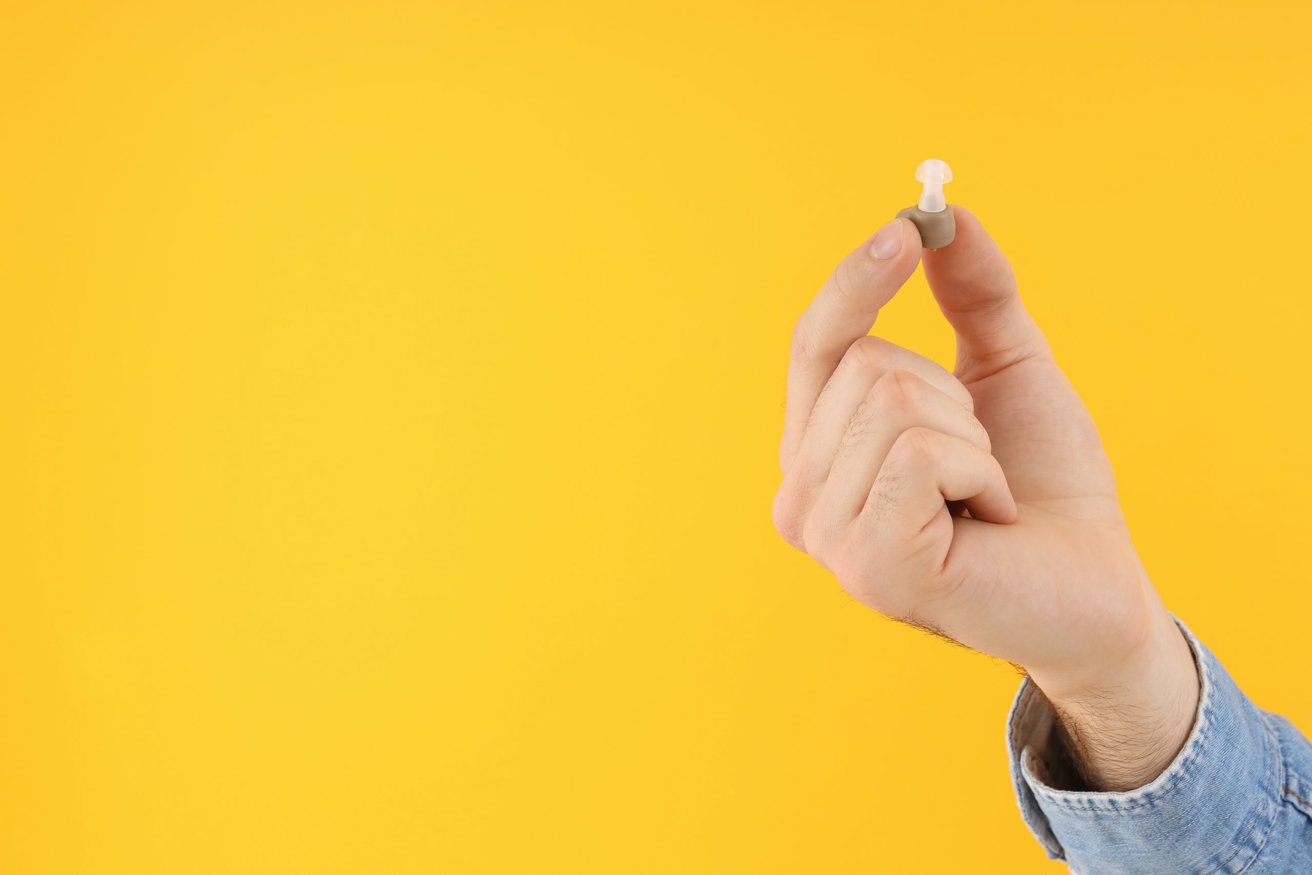 Male hand holds hearing aid on yellow background