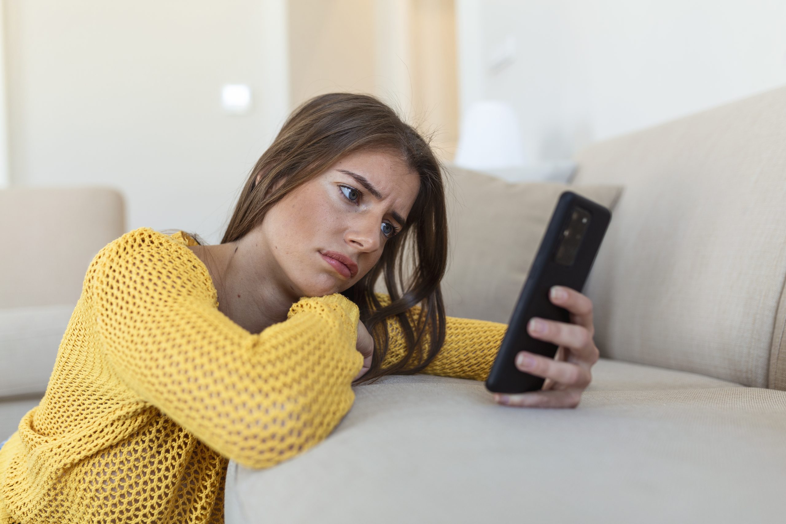 Pensive sad young woman holding smartphone waiting sms from boyfriend.