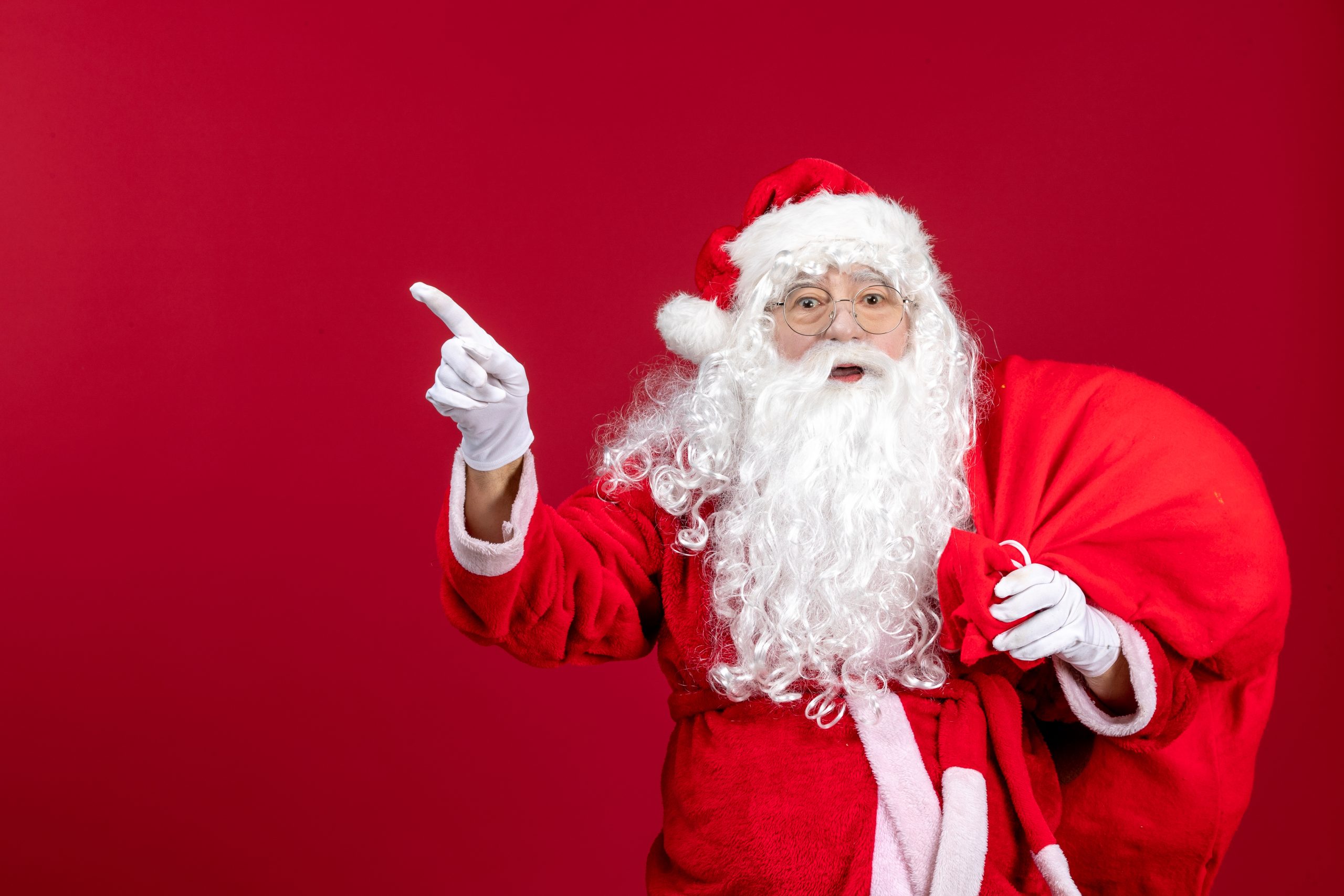 front-view-santa-claus-carrying-bag-full-of-presents-pointing-on-red-emotion-new-year-christmas-holiday